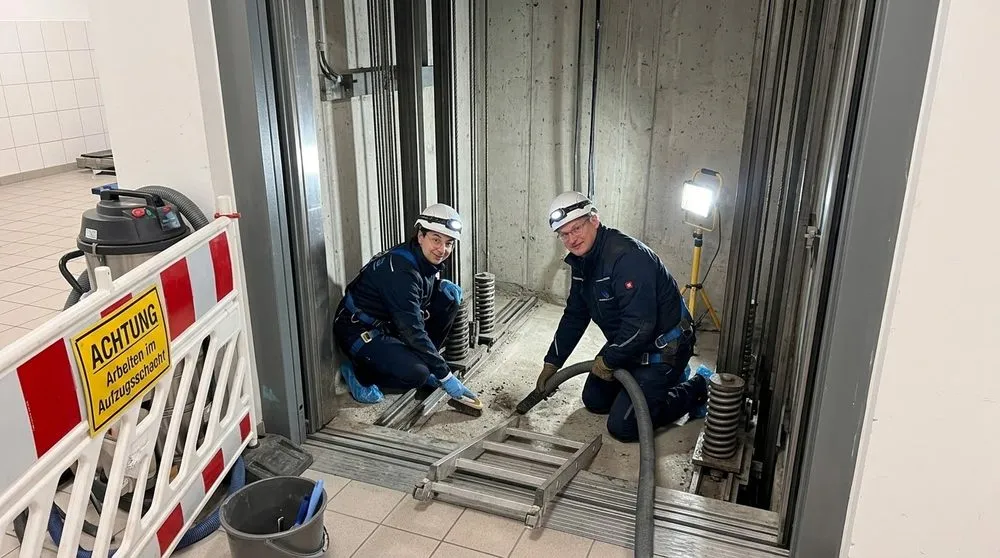 Zwei Mitarbeiter der VB Reinigungskonzepte reinigen mit Industriesauger und Bürste die Aufzugsgrube