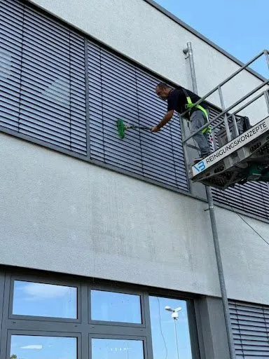 Mitarbeiter reinigt von der Arbeitsbühne aus Fassade und Lamellen eines Gebäudes